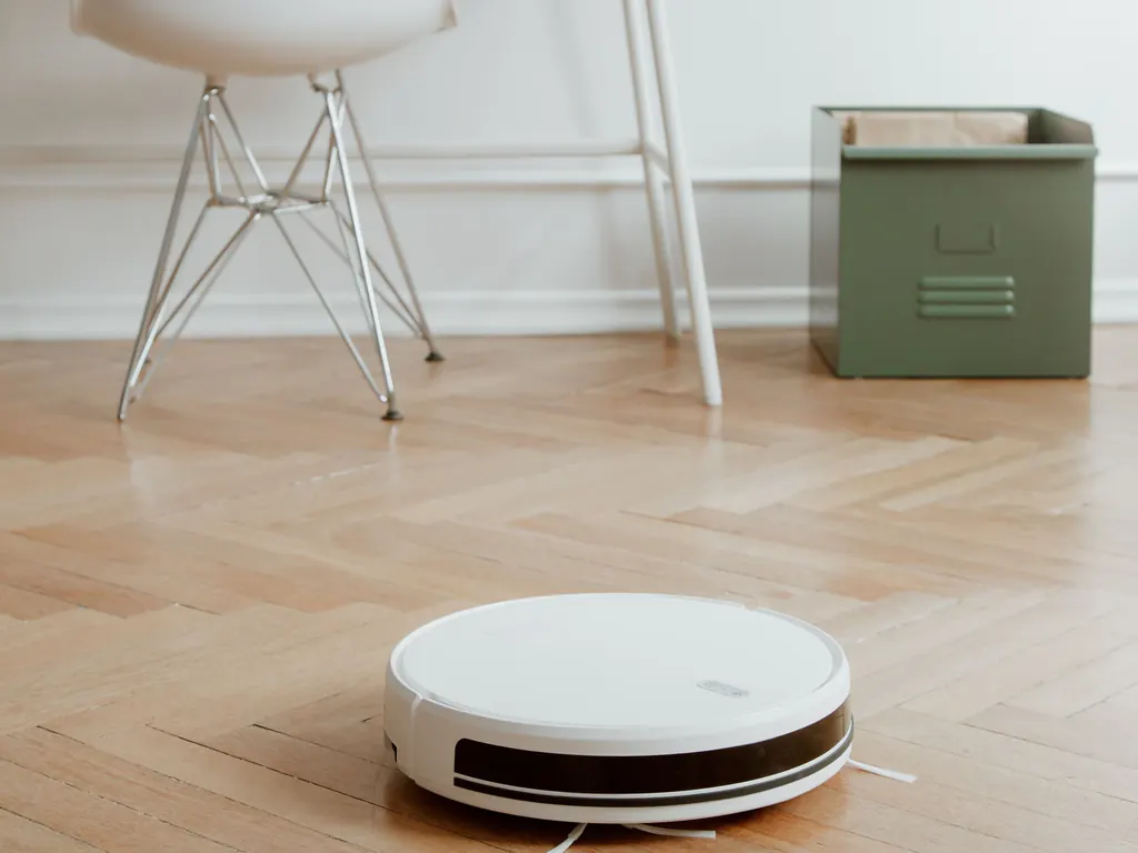 Robot hút bụi màu trắng trên sàn gỗ lát xương cá trong một căn phòng sáng